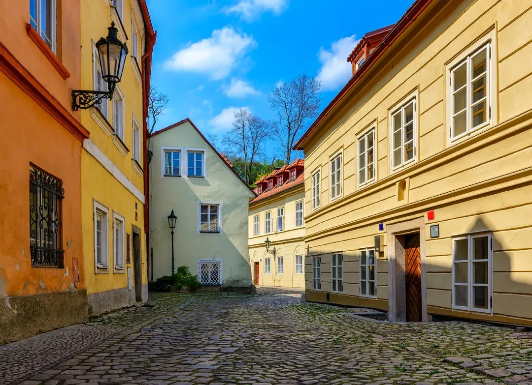 Úzká dlážděná ulice s barevnými domy a modrou oblohou.