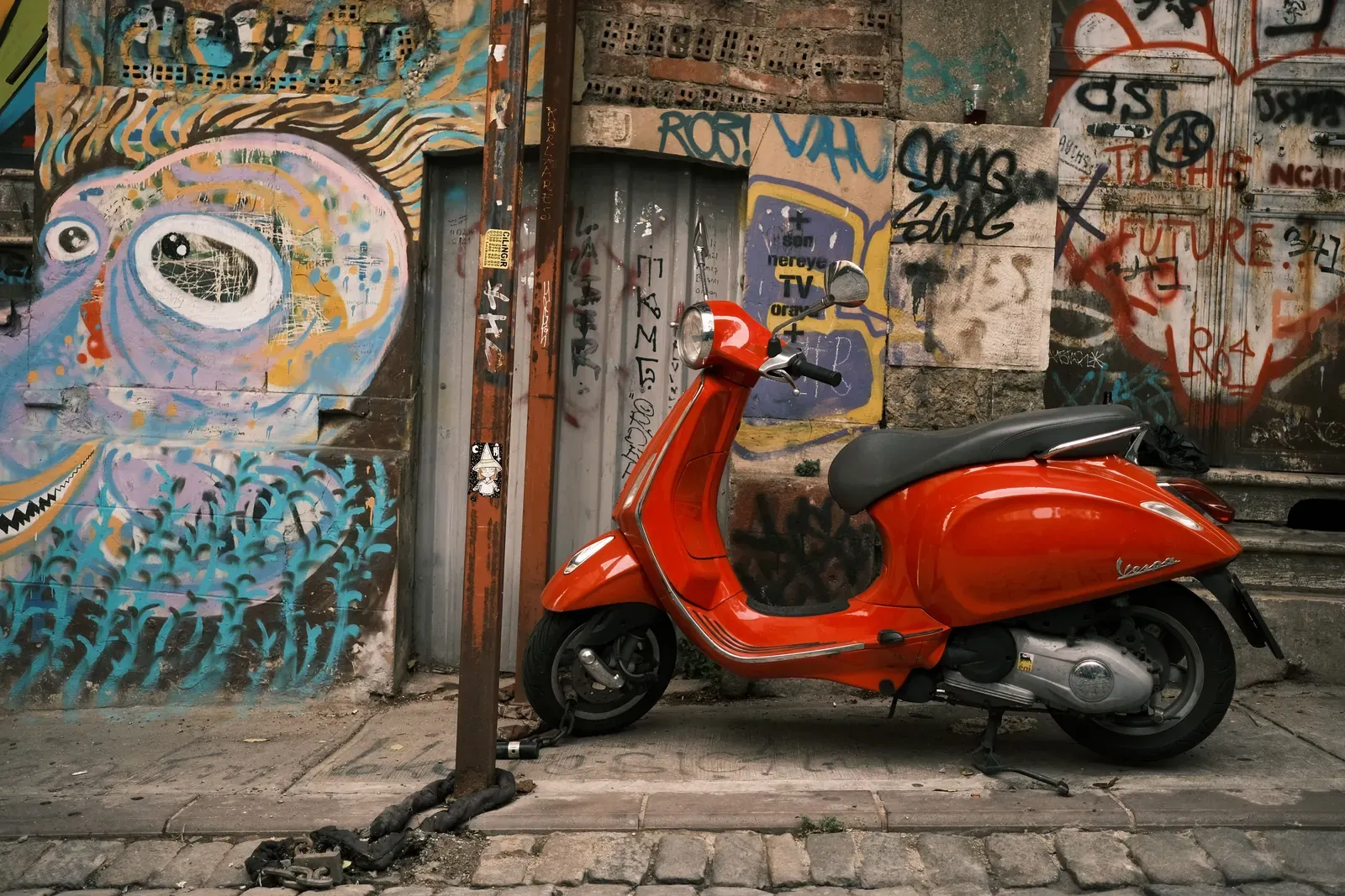 Červená Vespa zaparkovaná na chodníku před zdí s graffiti