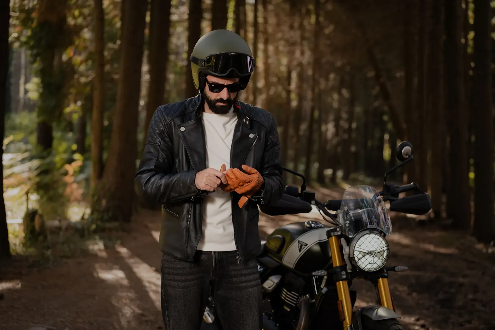 Motorkář v kožené bundě a helmě si upravuje rukavice vedle motocyklu