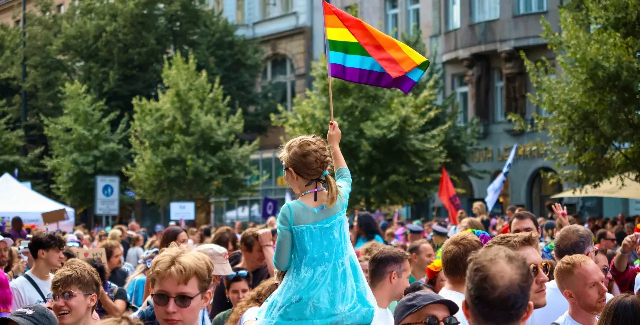 Děti v modrých šatech mávají duhovou vlajkou na pražském Pride průvodu.