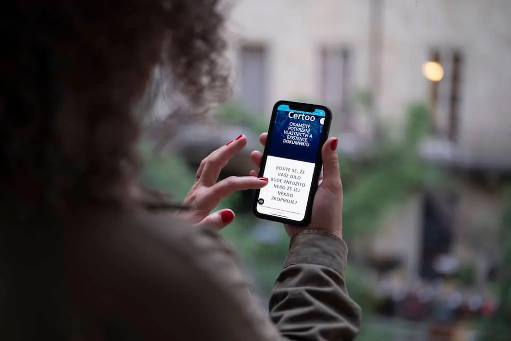 Osoba držící mobilní telefon s aplikací Certoo pro ochranu autorských práv.