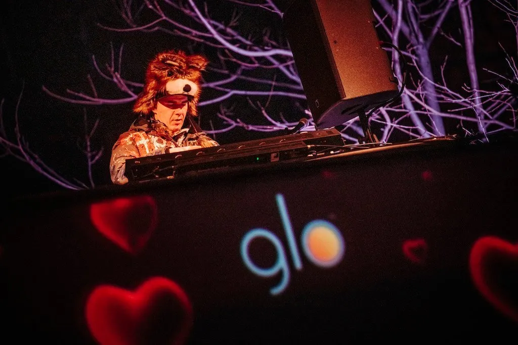 DJ Roxtar za DJ pultem, oblečený v barevném kostýmu s liščími ušima.