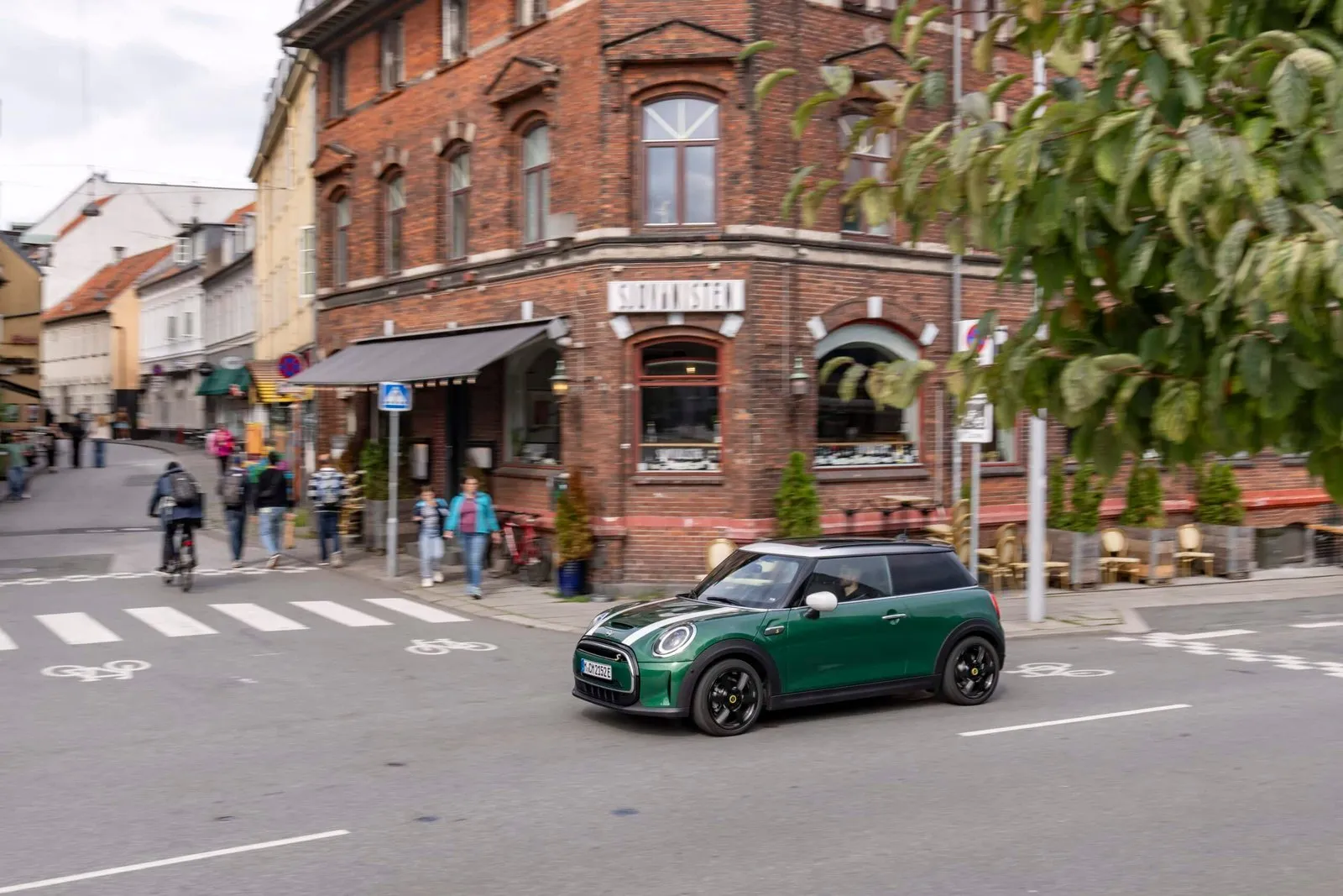 Zelené vozidlo MINI projíždí kolem historické budovy s restaurací.