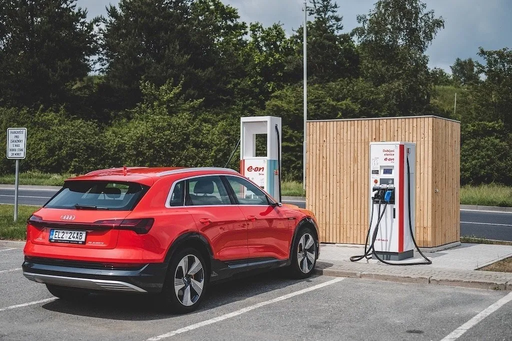 Červené elektrické SUV parkované u nabíjecí stanice na krajinném pozadí.