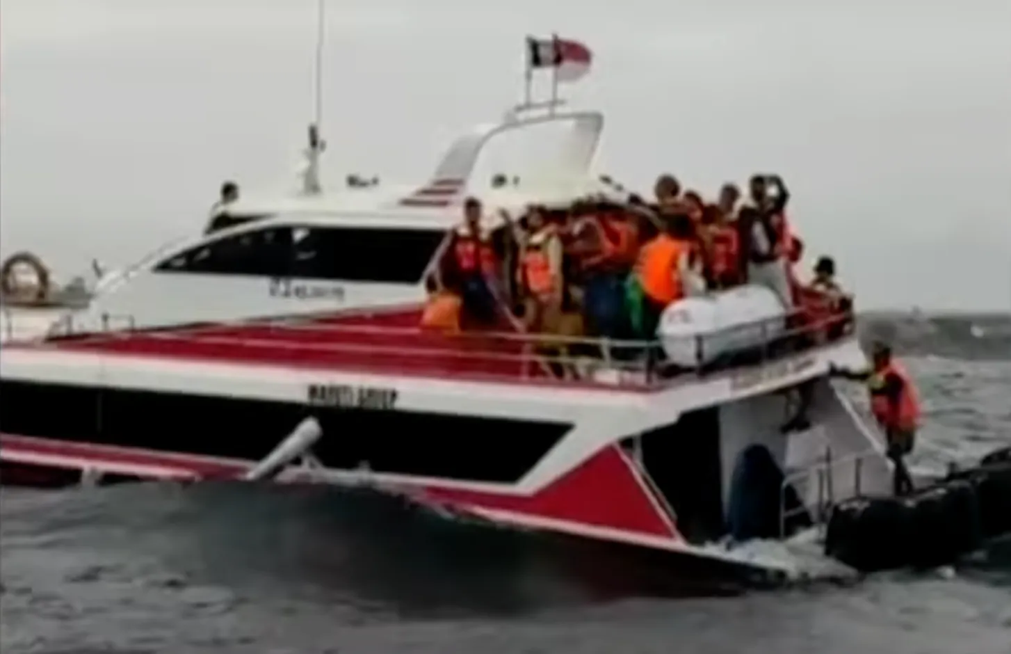 Nákladní loď s pasažéry v záchranných vestách na rozbouřeném moři.