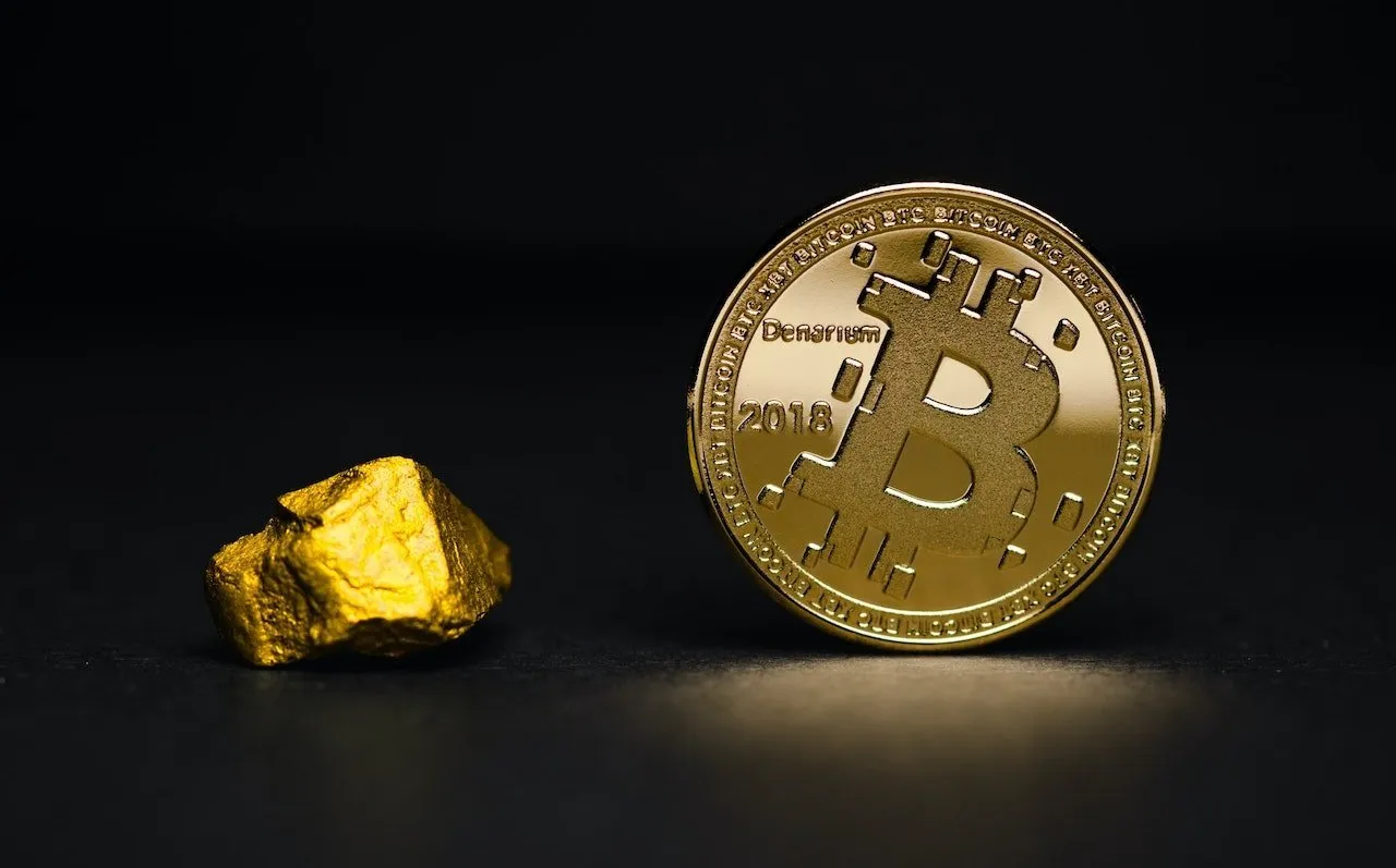 Zlatá Bitcoin mince vedle zlatého kamene na tmavém pozadí.
