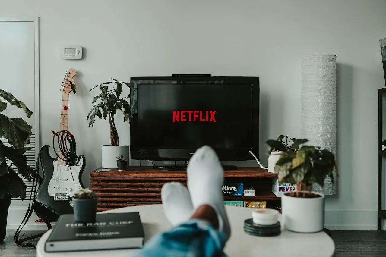 Osoba relaxuje s nohama na stole, sleduje Netflix na televizi.