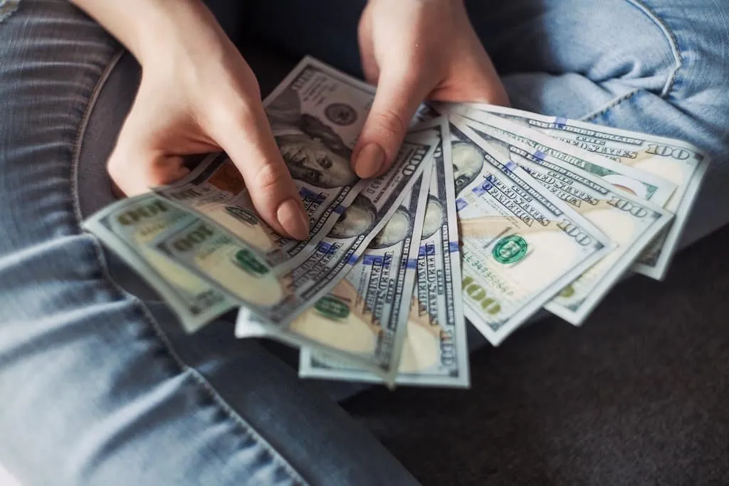 Osoba držící v rukou svazek bankovek s hodnotou 100 dolarů.