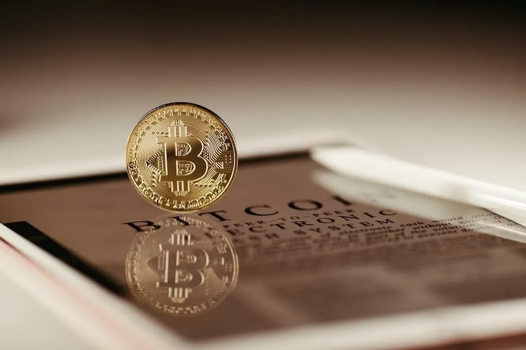 Zlatá bitcoinová mince levituje nad novinovým článkem o kryptoměnách.