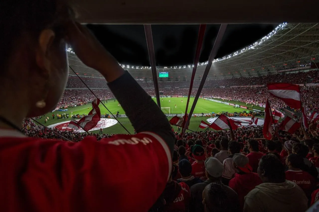 Fanoušci na stadionu s vlajkami, sledující fotbalový zápas.