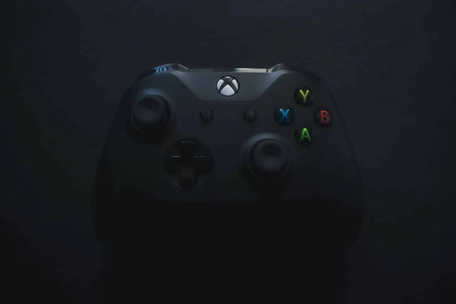 Černý herní ovladač Xbox s barevnými tlačítky na tmavém pozadí.